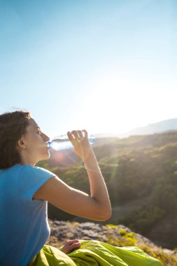 İçme suyu bir dağın tepesinde bir kadındır. Kız onun susuzluk quenches. Yorgun turistik bir plastik şişeden içer. Esmer günbatımında bir uyku tulumu içinde oturuyor.