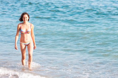 Bir kadın bir mayo içinde denizden geliyor. Kız okyanusta yüzüyor. Sahilde dinlenin. İnce esmer sahilde. Dalgalar deniz.