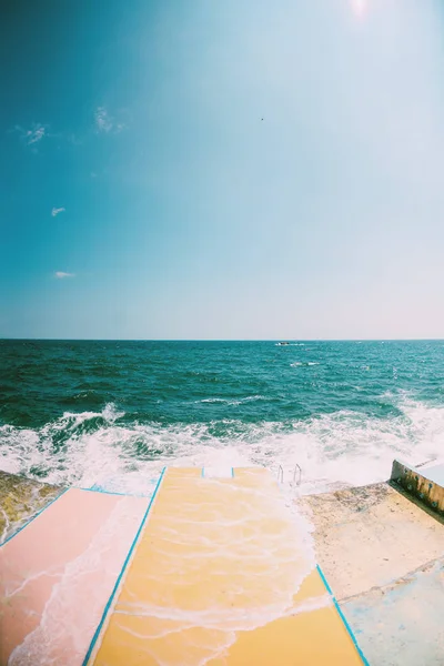 Pier on the waterfront. Sea waves break on the breakwater. Ocean landscape. Quay street resort town. Foam from sea water.