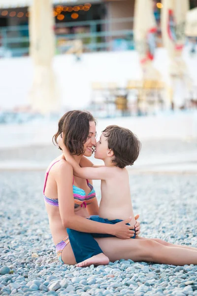 The boy hugs mom. Woman resting with her child on the beach. Mother\'s hugs. Woman playing with her son. Holidays with children on the coast.