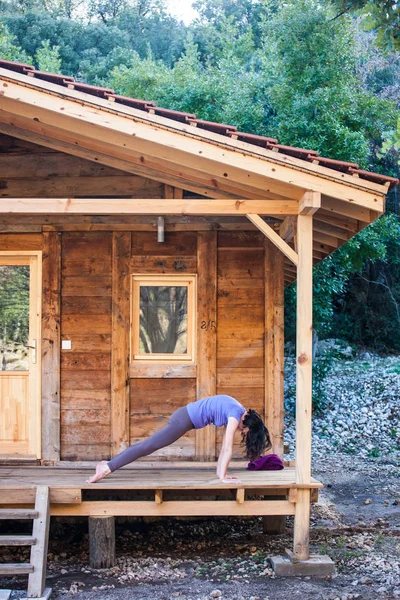 A woman practices yoga on the porch of an old wooden house. The girl goes in for sports in the yard on a warm spring day. Slender brunette doing asanas.