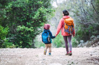 Bir kadın oğluyla birlikte ormanda yürüyor. Annesiyle yürüyüşe çıkan çocuk. Sırt çantalı bir çocuk parkta. Çocuklarla seyahat et. Çocuk annesinin elini tutuyor..
