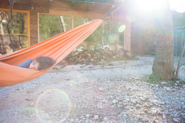 少年はハンモックに寝そべっている 子供は自然の中で休んでいる 木造住宅の近くのハンモック — ストック写真