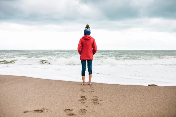 赤脚的女人看着冬天的大海 在阴天 戴帽子的女孩沿着海边散步 一个女人在冷水中织布 秋日的波浪和天空 — 图库照片