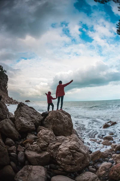 一名女子带着儿子站在石头上 望着大海 那个男孩和他妈妈看着海浪 这孩子正沿着海边走着 妈妈和孩子的剪影反对天空 — 图库照片