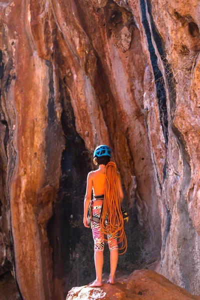 Climber holds the rope and prepares to overcome the route. Slender girl holds climbing equipment. A woman in a helmet looks at a rock wall.