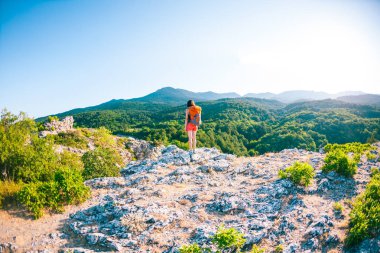 Dağın zirvesine kıza. Bir kadın bir sırt çantası ile bir dağ yolunda yürüyor. Yukarı tırman. Güzel yerlere seyahat. Gökyüzü ve deniz karşı Turizm.