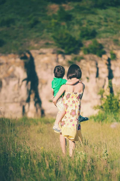 母亲拥抱了这个男孩 一名女子正和儿子一起穿过田野 孩子坐在母亲的怀里拥抱她 妈妈的拥抱 — 图库照片