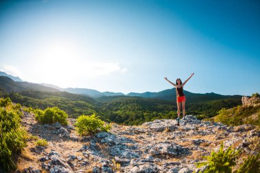Dağın zirvesine kıza ellerini kaldırdı. Kadın için üst tırmandı ve onun başarı zevk. Batan güneşin ışınları. Esmer yükselen güneş ağırlıyor.