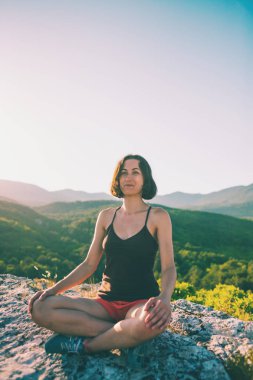 Bir kız bir dağın tepesinde oturan ve gülümseyerek. Bir kadın doğanın güzelliği hayran. Güzel yerlere seyahat. Turist gökyüzüne karşı. Ufuk esmer bakar.