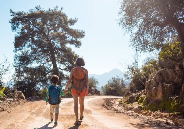 Çocuk annesi ile bir dağ yolda yürür..