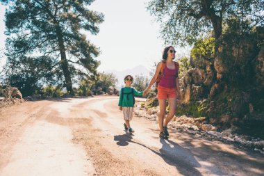 Çocuk annesi ile bir dağ yolda yürür..