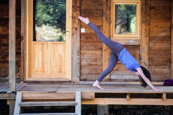 Una donna pratica yoga sotto il portico di una vecchia casa di legno . — Foto Stock