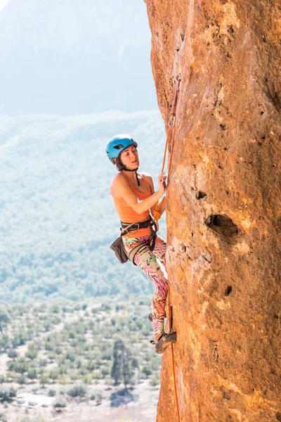 Una chica en un casco sube a una roca . — Foto de Stock