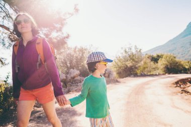 Çocuk annesi ile bir dağ yolda yürür..