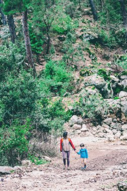 Çocuk annesi ile bir dağ yolda yürür..
