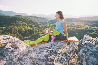 Bir gezgin bir dağın üstünde otururken kahve içiyor.