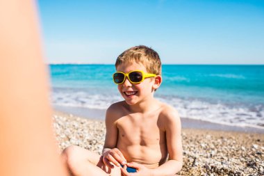 Güneş gözlüğü içinde bir çocuk sahilde oynuyor.