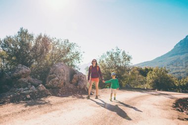 Çocuk annesi ile bir dağ yolda yürür..