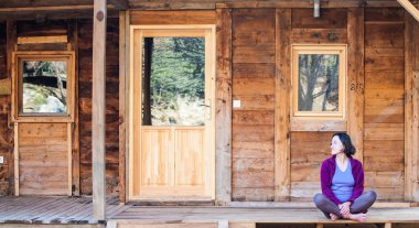 Bir kadın eski bir ahşap ev verandada oturuyor.