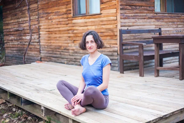 Eine Frau sitzt auf der Veranda eines alten Holzhauses. — Stockfoto