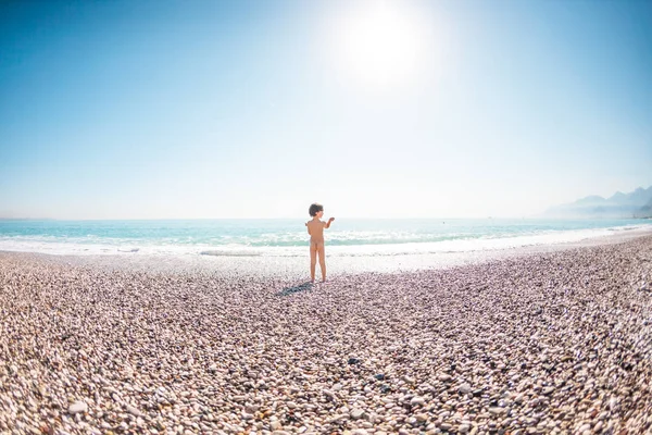 Un niño se para en la playa y mira al mar . — Foto de Stock