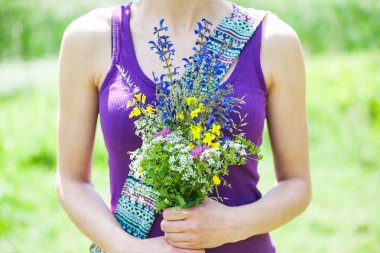 Kız elinde bir buket kır çiçeği tutuyor..