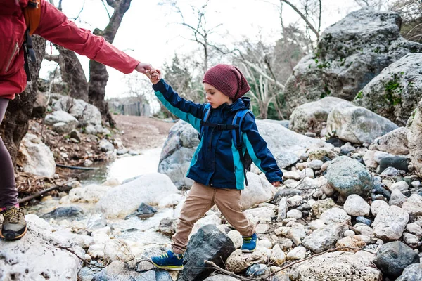Жінка допомагає дитині перетнути гірську річку . — стокове фото