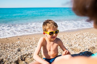 Güneş gözlüğü içinde bir çocuk sahilde oynuyor.