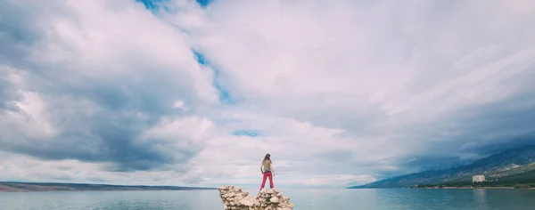 La chica se para sobre un montón de piedras y mira al mar . — Foto de Stock