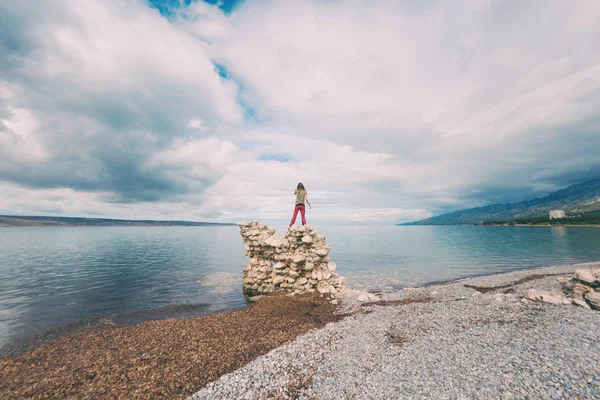 Het meisje staat op een stapel stenen en kijkt naar de zee. — Stockfoto
