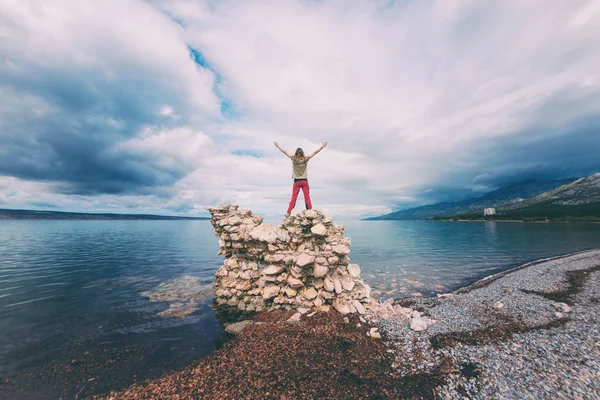 Het meisje staat op een stapel stenen en kijkt naar de zee. — Stockfoto