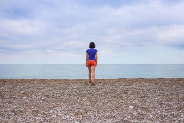 Bir kadın yalnız deniz kıyısında yürür.