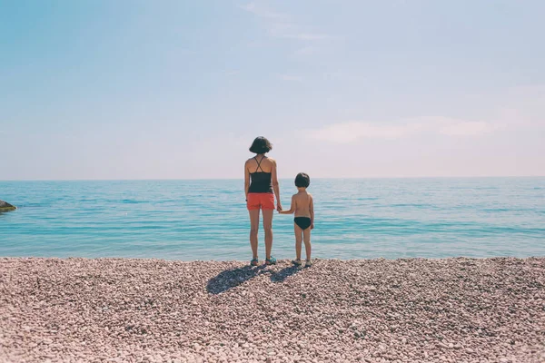 Un ragazzo con sua madre in piedi sulla spiaggia e guardando il mare . — Foto Stock