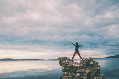 Kız taş yığını üzerinde duruyor ve denize bakıyor.