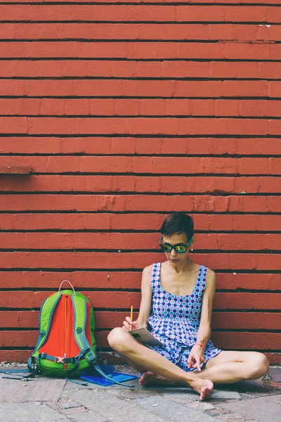 Yalınayak kız bir tuğla duvara yakın oturan çizer. — Stok fotoğraf