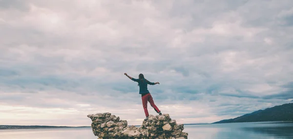 La chica se para sobre un montón de piedras y mira al mar . — Foto de Stock