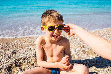 Güneş gözlüğü içinde bir çocuk sahilde oynuyor.
