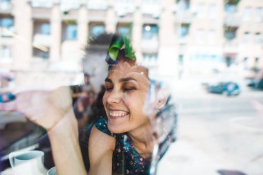 Gülümseyen kız bir kafede oturan ve pencereden dışarı bakıyor.