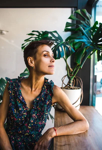 Ragazza sorridente seduta in una caffetteria e che guarda fuori dalla finestra . — Foto Stock