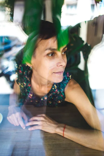 Ragazza sorridente seduta in una caffetteria e che guarda fuori dalla finestra . — Foto Stock