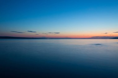 Deniz ve gökyüzü bulutlu gün batımında.