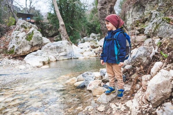 Un enfant avec un sac à dos se tient près d'une rivière de montagne . — Photo
