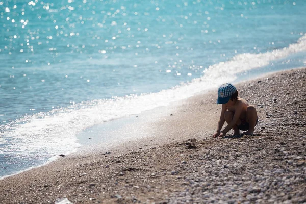 Chico jugando con guijarros en la playa . — Foto de Stock