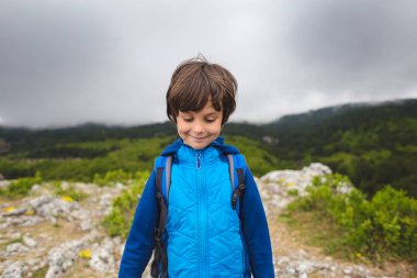 Sırt çantası olan bir çocuk dağın tepesinde duruyor..