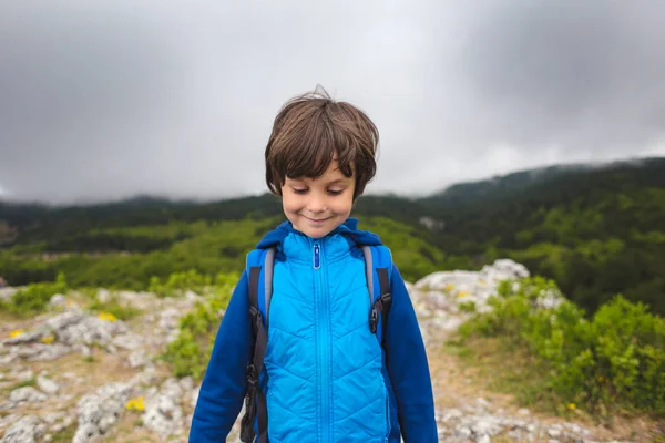 Un niño con una mochila se para en la cima de una montaña . — Foto de Stock