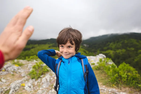 Um menino com uma mochila subiu ao topo da montanha e dá cinco . — Fotografia de Stock