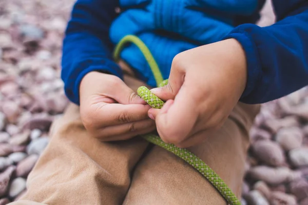 A child learns to knit a knot from a rope.