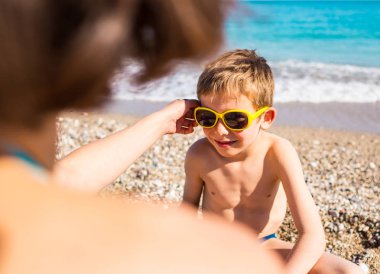 Güneş gözlüğü içinde bir çocuk sahilde oynuyor.