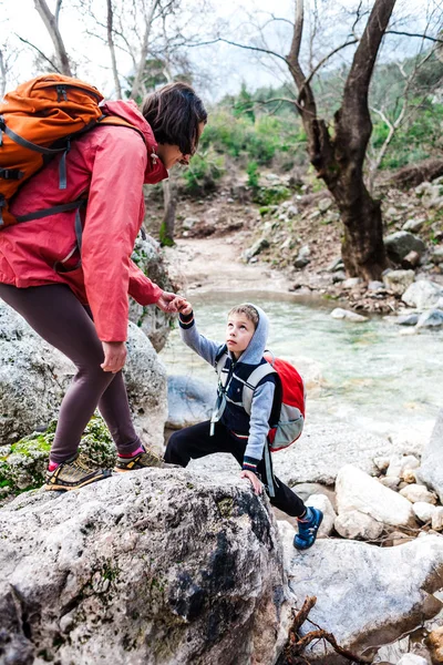Kobieta pomaga dziecku przekroczyć górskiej rzeki. — Zdjęcie stockowe